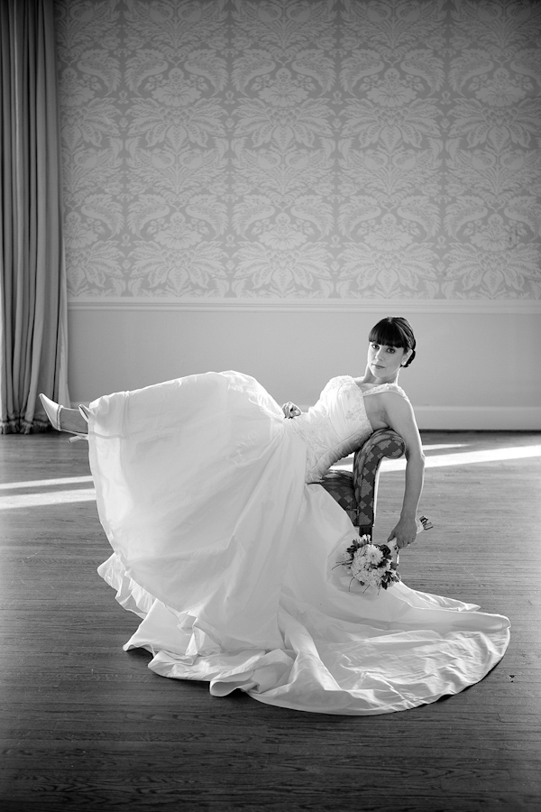 black and white photo - beautiful bride wearing a ball gown style dress lounging in chair in the middle of a ballroom - photo by North Carolina based wedding photographers Cunningham Photo Artists